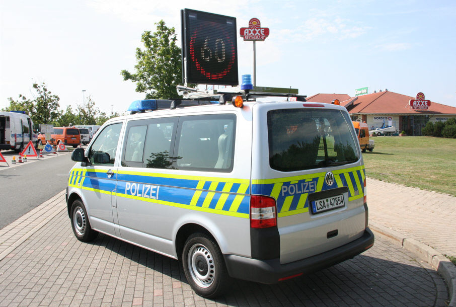 polizeiliches Sicherungsfahrzeug mit Geschwindigkeitsbegrenzungstafel